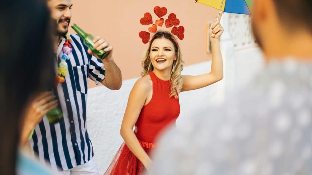 A woman in a red dress and heart headband smiles while holding a small umbrella.