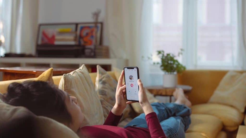 A woman lying on a couch using a dating app on her phone.