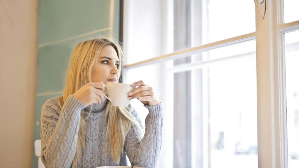 A woman holding a cup and looking out a window.