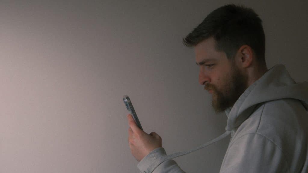 A man with a beard looks down while holding and checking a mobile phone.