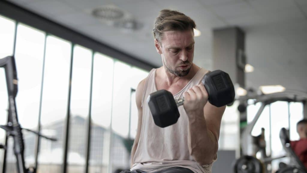 A man in a tank top lifts a heavy dumbbell in a gym.