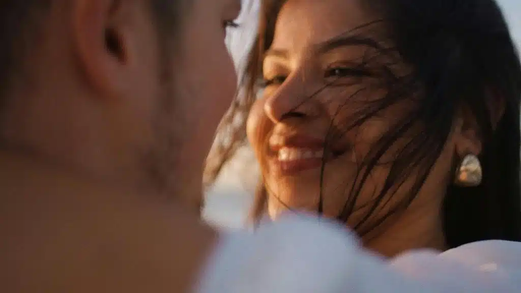 A woman smiling warmly at someone with wind blowing through her hair.
