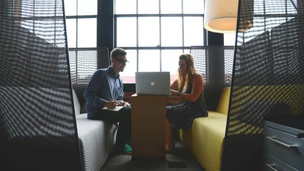 A man and woman working together on a laptop in a booth.