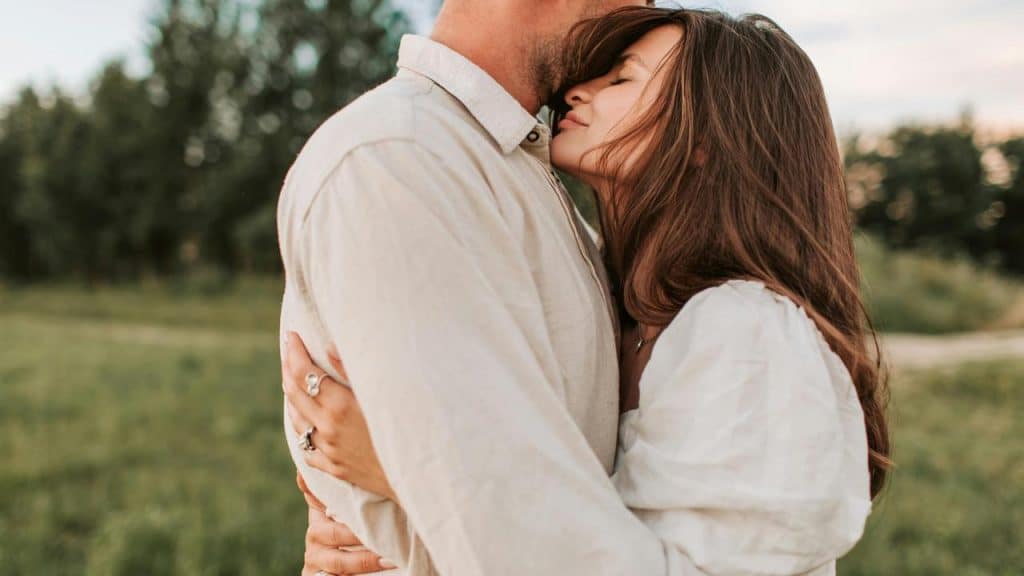 A woman hugging a man and resting her head on his chest outdoors.