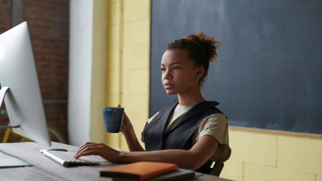 A woman working at a computer while holding a coffee mug.