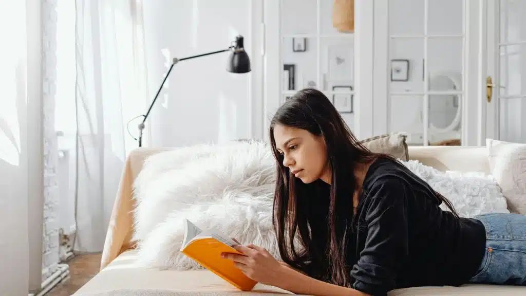 A woman lying on a couch reading a book.