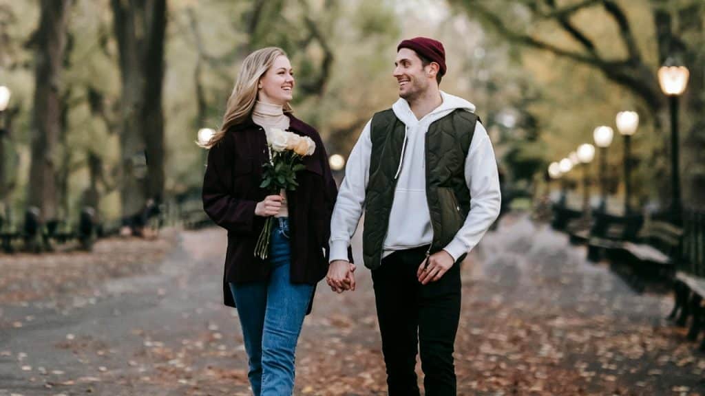 A couple holding hands and walking together outdoors in a park, woman holding flowers.