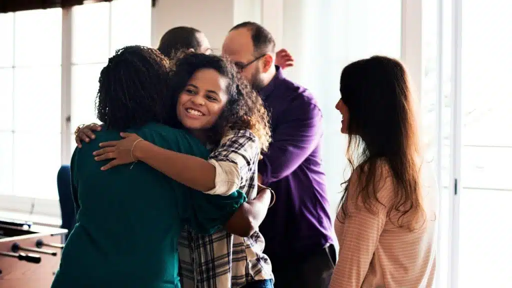 A woman in a plaid shirt smiles while hugging another person in a group.