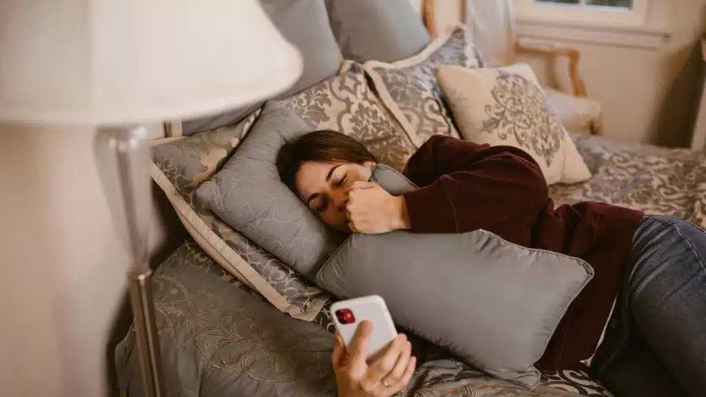 A woman lying on a bed holding a pillow and looking at her smartphone