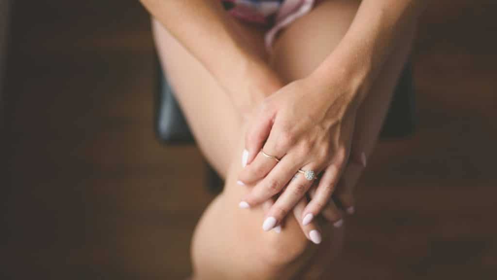 Close-up of a person’s hands resting on their lap, wearing two rings with white nails.