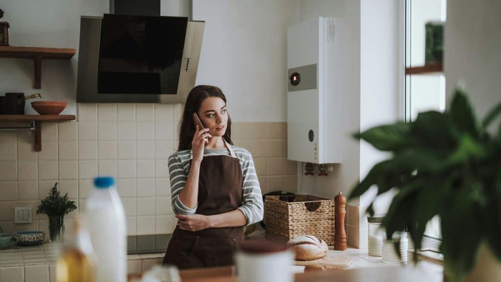 A woman in an apron talking on the phone in a kitchen.