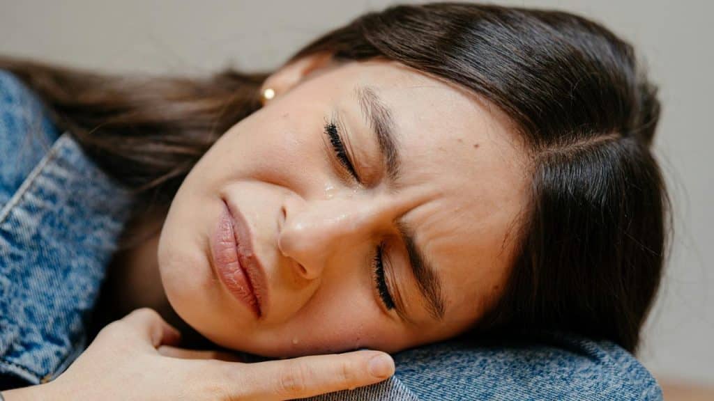 A close-up of a woman lying down with tears on her face, appearing sad.
