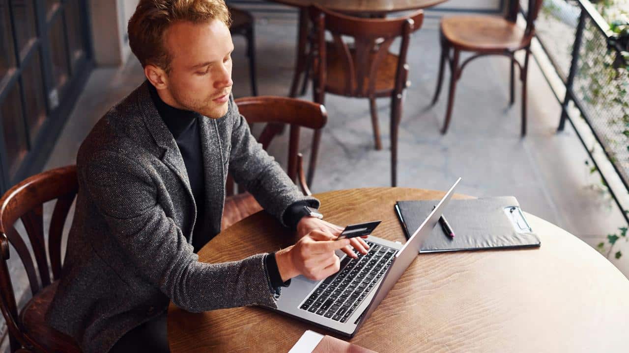A man uses a laptop and holds a credit card at a cafe table.