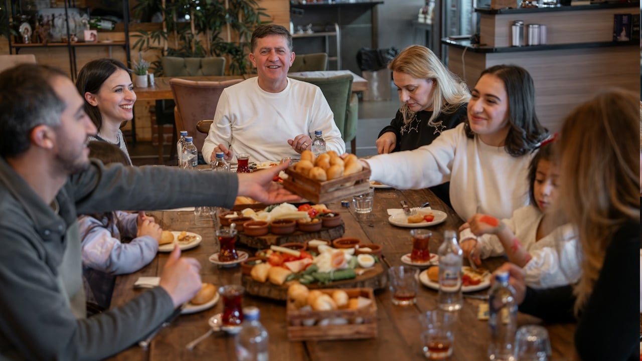 Group of people dining around a long table Passing food and drinks