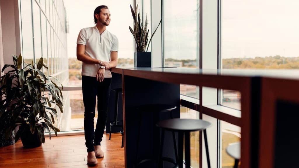 A man standing by a large window in a modern office, looking outside.