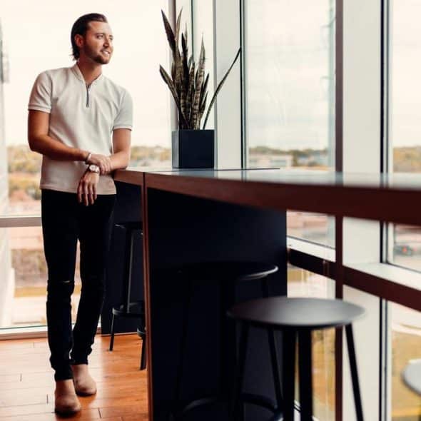 A man standing by a large window in a modern office, looking outside.