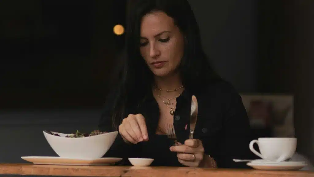 A woman sitting at a table eating a salad with a cup of coffee nearby.