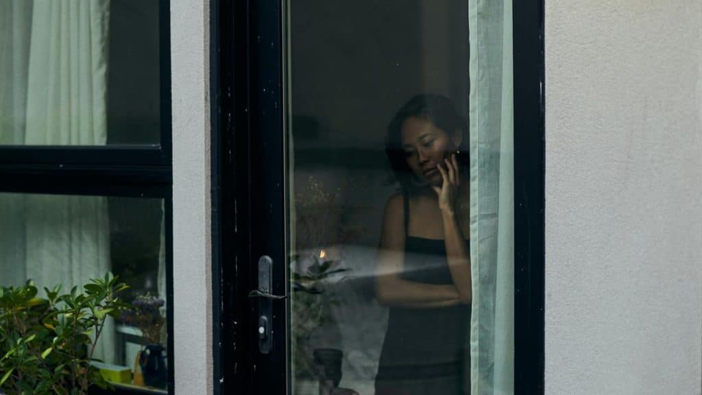 A woman looking out a window with a sad expression.