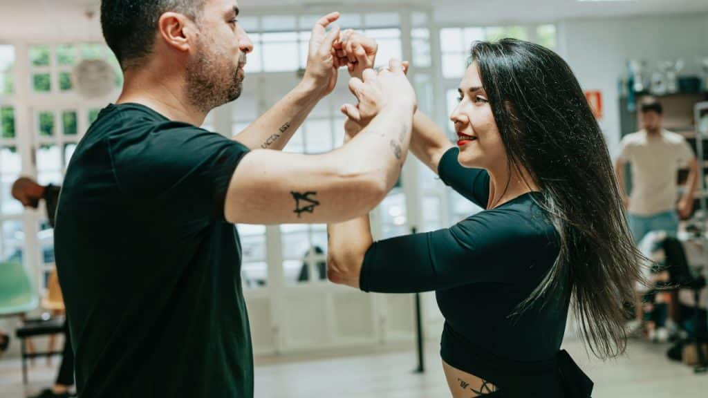 A man and woman face each other while holding hands high during a partner dance.
