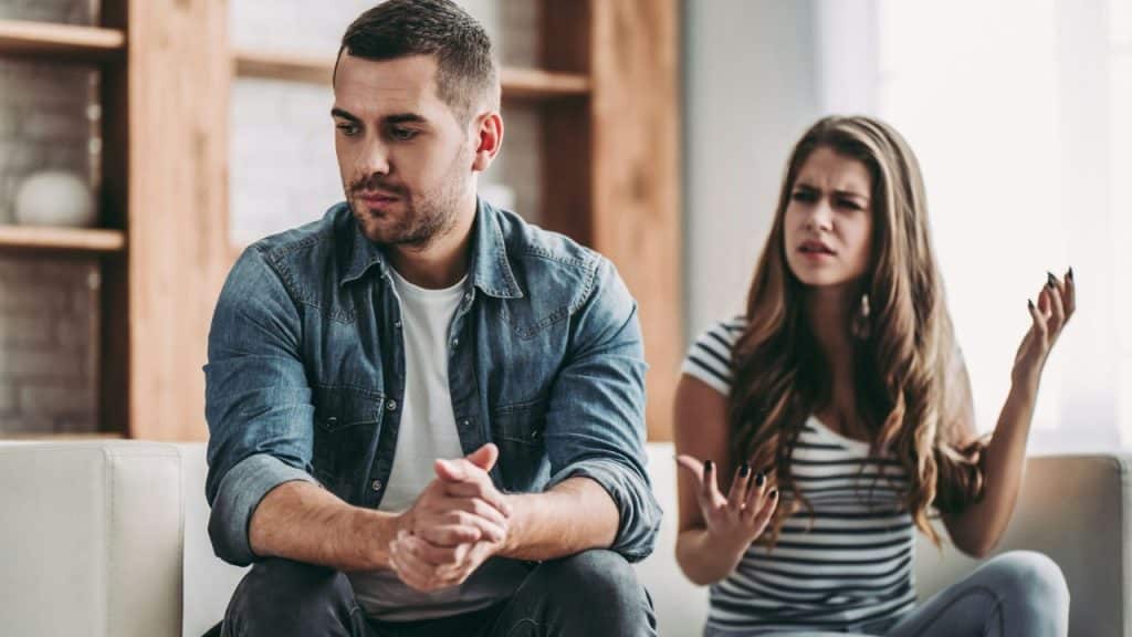 A man looks away while a woman behind him gestures with her hands while speaking.