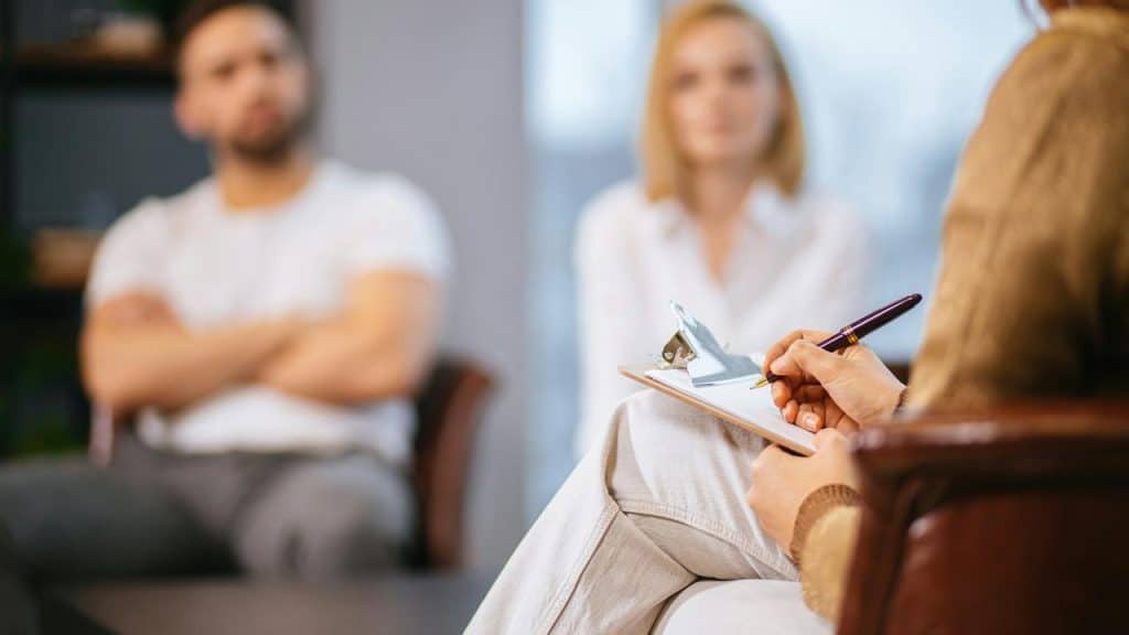 A therapist taking notes while a couple sits together during a counseling session.