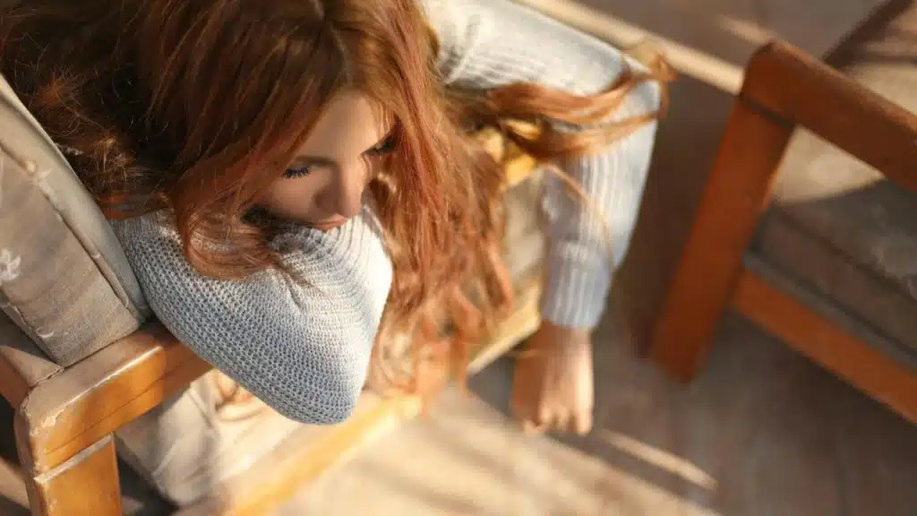 A woman with long red hair sitting pensively in a chair