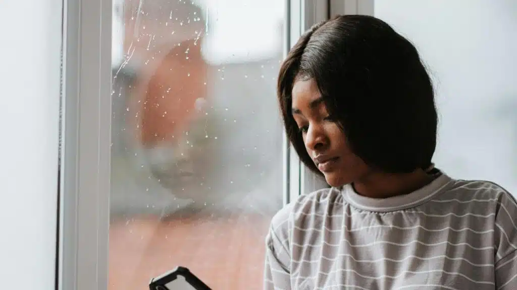 A woman looking at her phone by a rainy window.