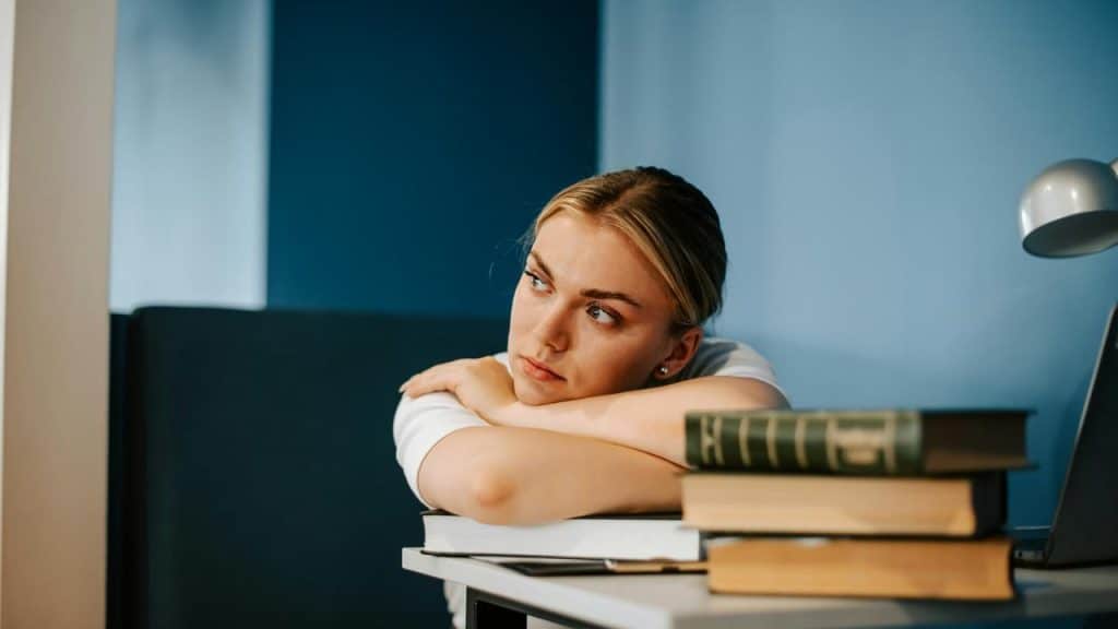 A woman resting her head on her arms beside a stack of books.