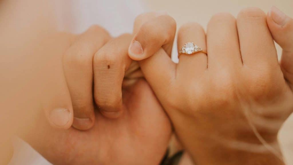 A close-up of two hands holding pinkies, one wearing an engagement ring