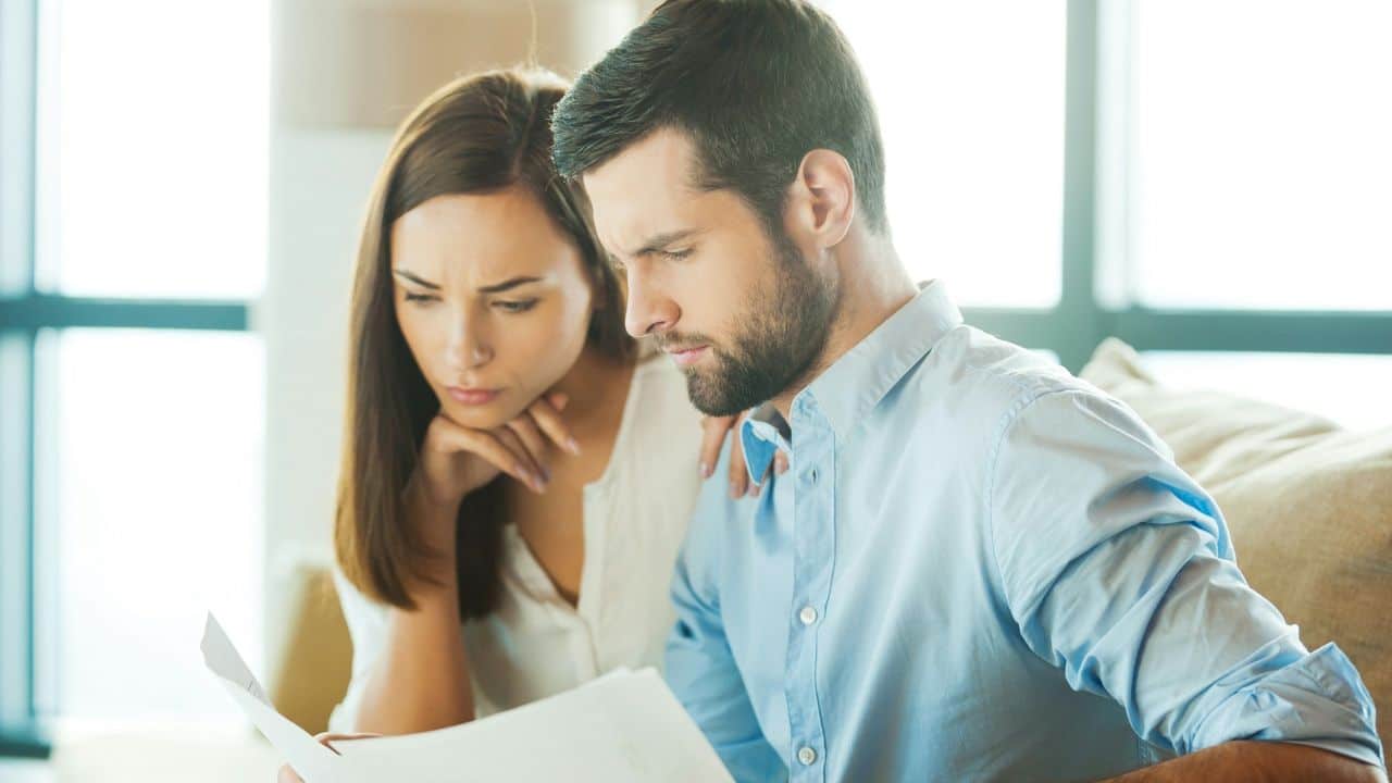 A man and woman sit together, both looking with focused concern at a white paper.