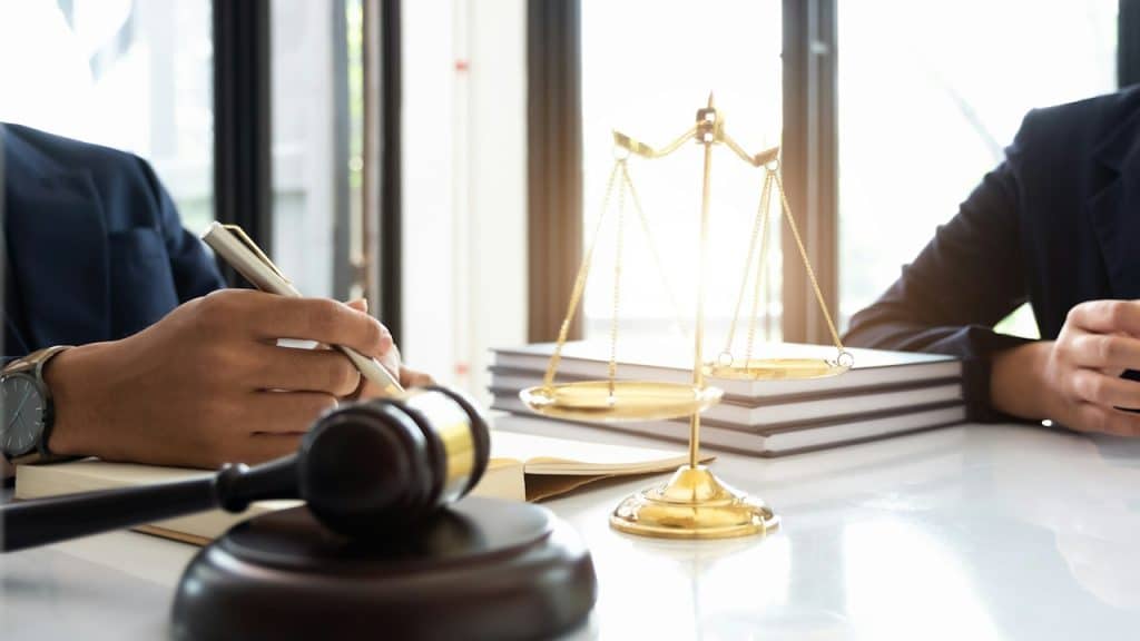 Two men sitting at a table on which scales and a gavel are placed.