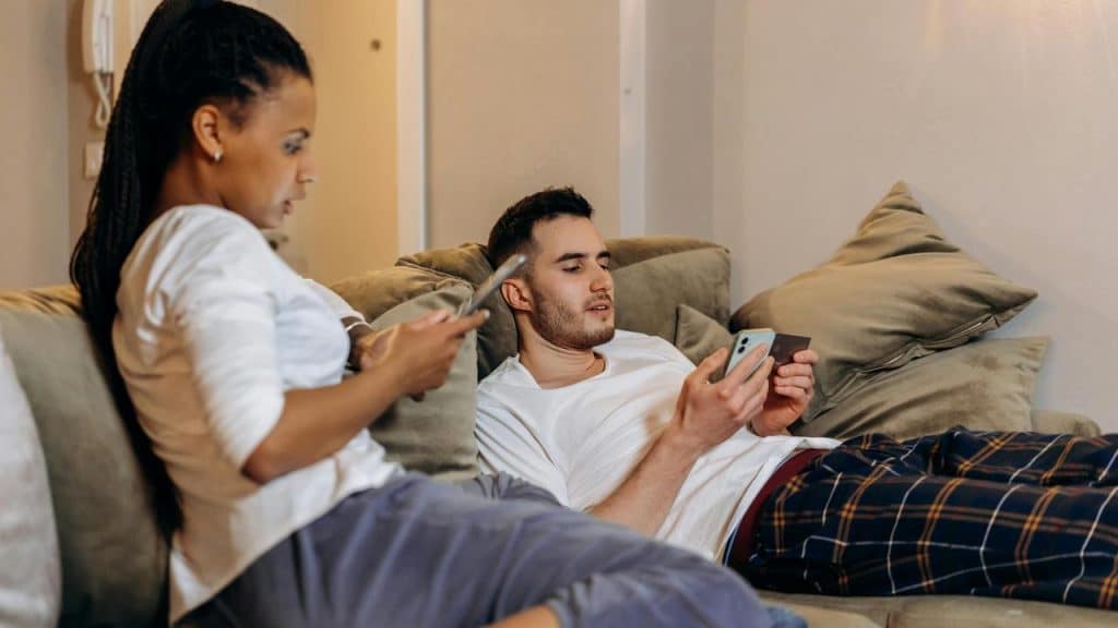A couple relaxing on a couch while using their smartphones.