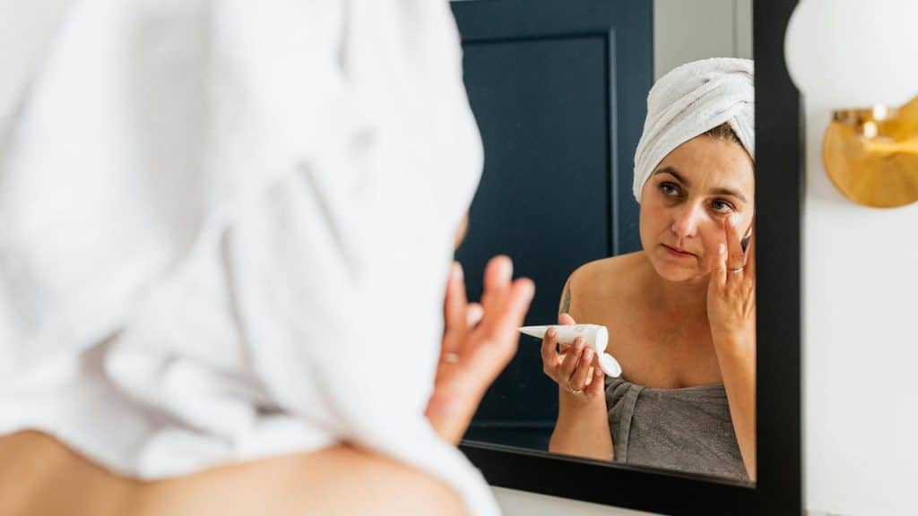 A woman applying skincare cream while looking in the mirror.