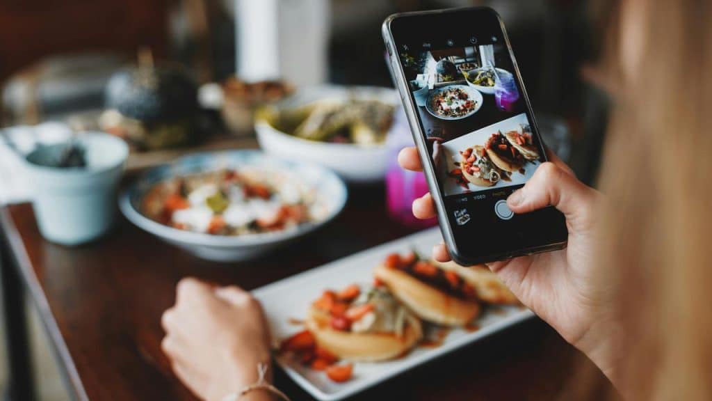 A person taking a photo of food with a smartphone at a restaurant table.