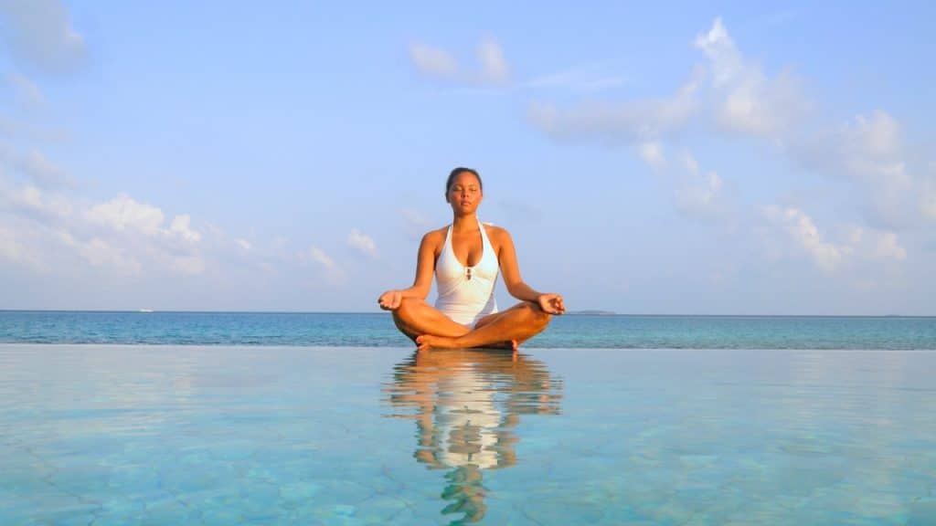 A woman meditating by an infinity pool overlooking the ocean.