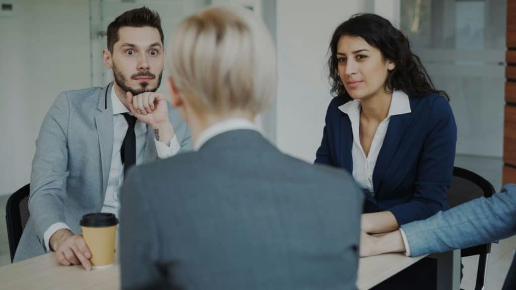 Three people in business attire sit together at a table during a meeting.