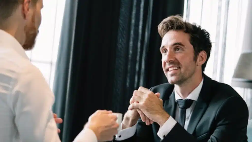 A man in a suit smiling while talking to another person holding a cup.