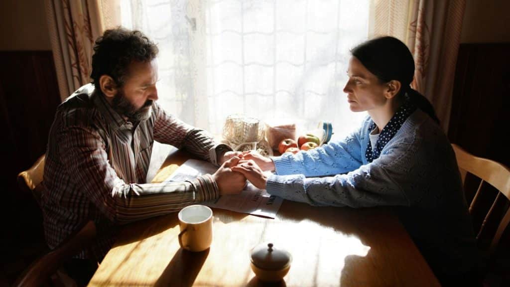 A man and woman sit at a table holding hands and looking directly at each other.