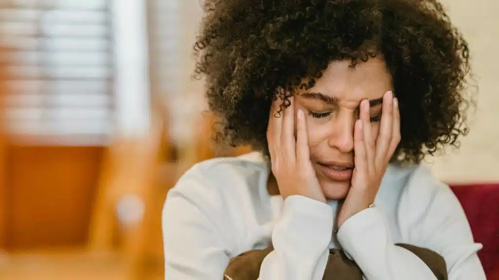 A woman sitting with her hands covering her face, appearing upset or stressed.