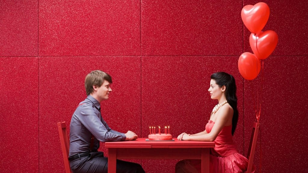 A man and woman sitting at a table with red balloons.