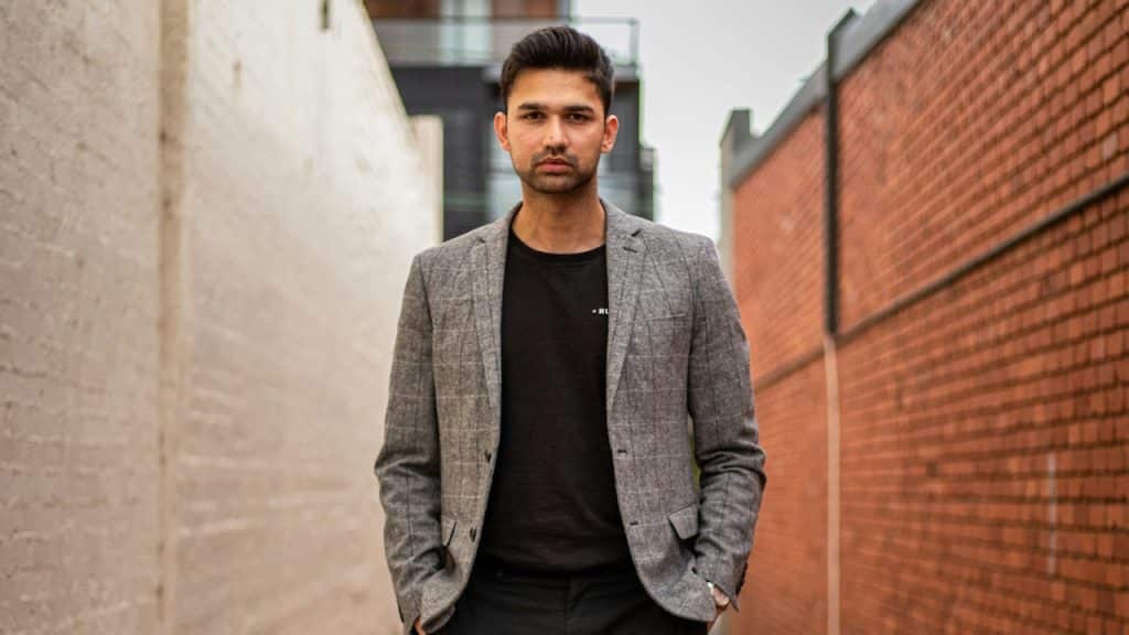 A man in a gray suit jacket and black pants standing on a brown concrete pathway during the daytime.