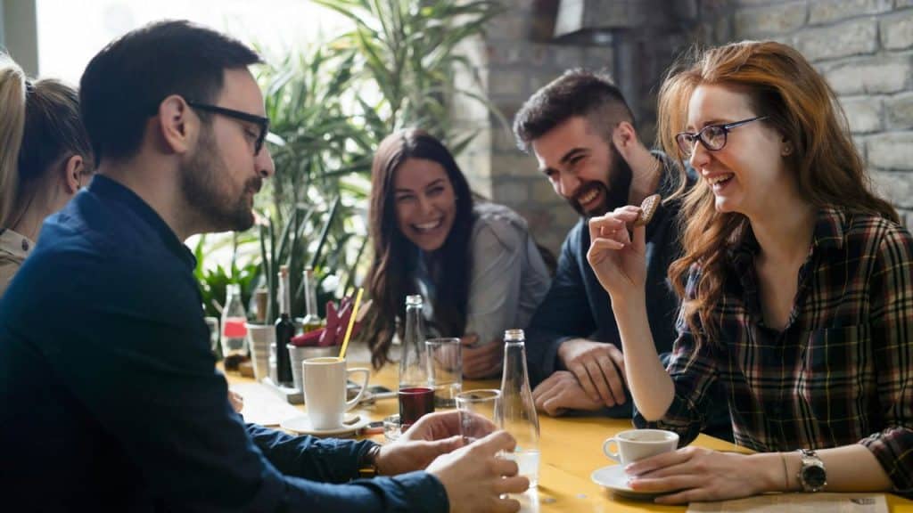 A group of four people sit around a wooden table talking and laughing together.
