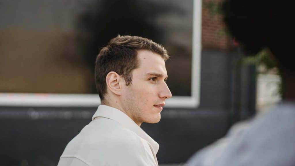 A young man in a light jacket looking to the side outdoors.