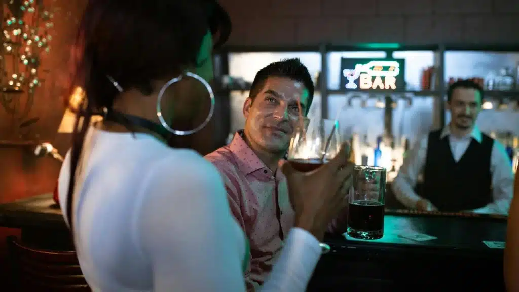 A woman holding a drink while talking to a man at a bar.