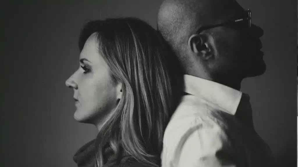 An upset couple standing with their backs touching.