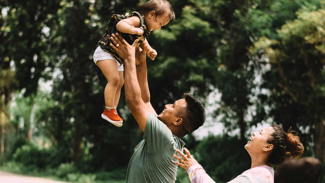 A happy couple playing with their baby outdoors.