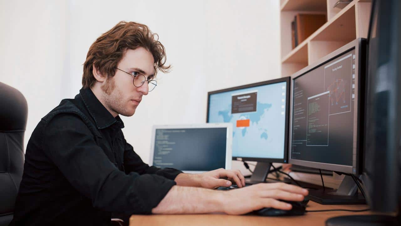 A man works on multiple computer screens at a desk.
