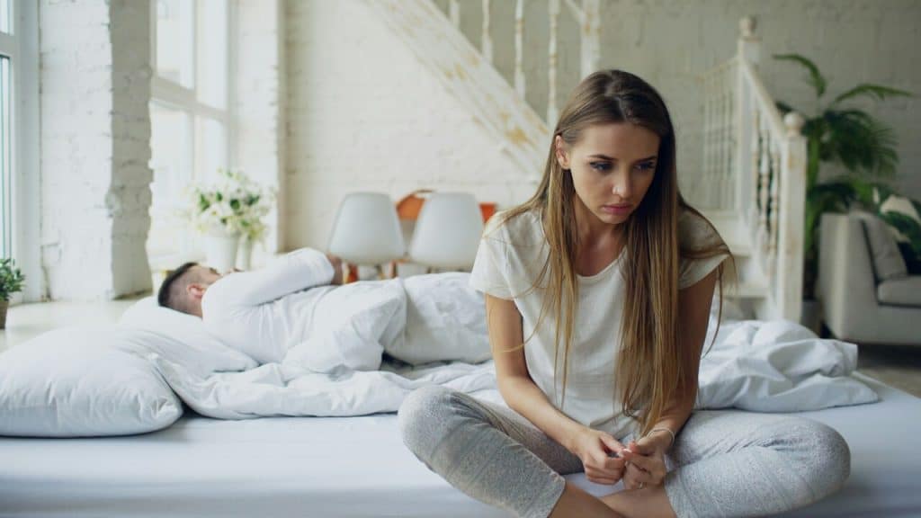 A woman looking sad while her husband sleeps