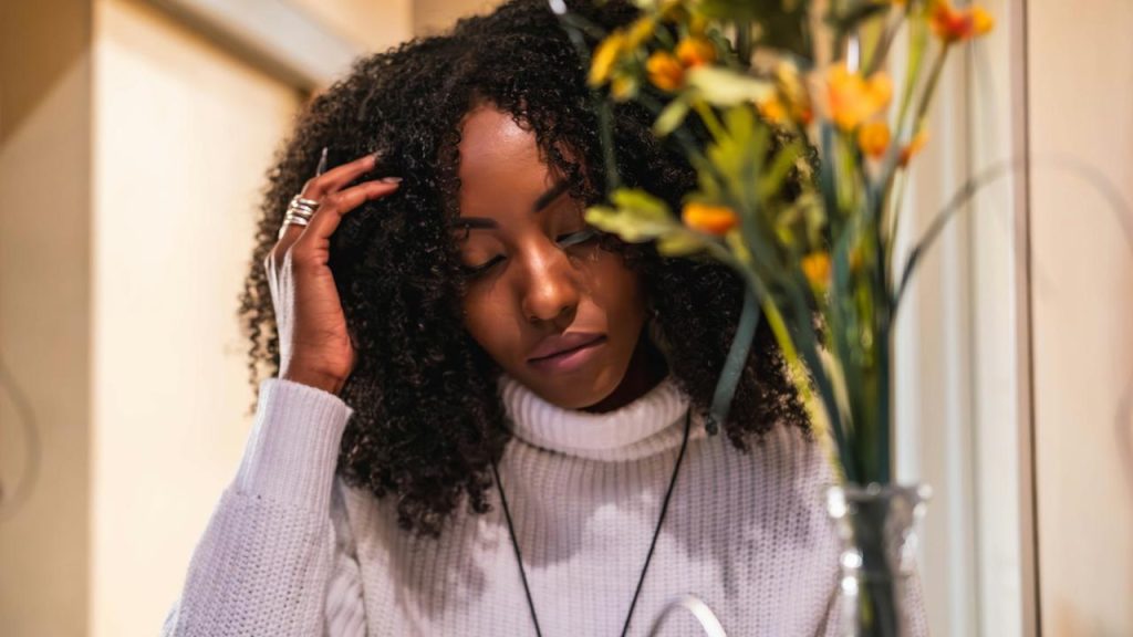 A woman with curly hair sitting beside a vase of flowers.