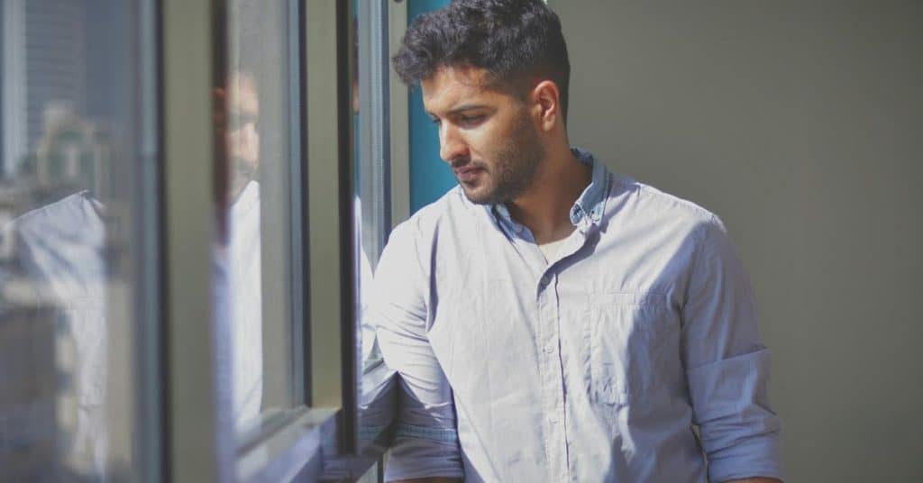 A man standing by a window, looking outside thoughtfully.
